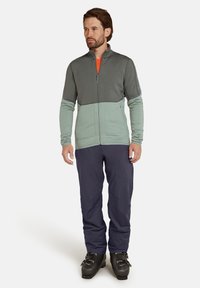 Heren zip-up jack in donkergrijs en lichtgroen, met een gestructureerde stof, gecombineerd met bijpassende marineblauwe broek en zwarte laarzen.