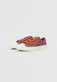 Sneakers in dark purple fabric with orange laces and accents. Features a white rubber toe cap and textured outsole.