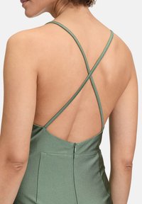 Zielona satynowa sukienka z krzyżującym się tyłem, cienkimi ramiączkami i dyskretnym zapięciem na suwak z tyłu. Gładka faktura z delikatnym połyskiem.