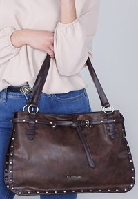 Borsa a mano in pelle marrone con hardware argentato, presenta dettagli borchiati, spallacci regolabili e un particolare cinturino annodato nella parte superiore.