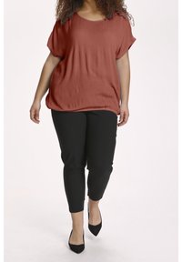 Rostfarbenes, kurzärmliges Oberteil mit strukturiertem Finish, kombiniert mit eng anliegenden schwarzen Hosen und spitzen schwarzen Absätzen, die eine lässige Silhouette schaffen.