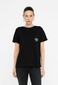 T-shirt nera a maniche corte con taschino sul petto e dettaglio del logo in strass. Realizzata in tessuto morbido con una vestibilità rilassata e un design minimal.