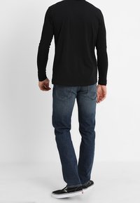 Camiseta negra de manga larga, diseño ajustado. Jeans de mezclilla azul con corte recto y desgaste sutil. Zapatillas negras de skate con suelas blancas.