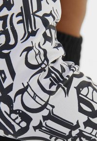 Černobílé legíny s abstraktním grafickým designem, který obsahuje tučné, stylizované písmo na hladkém, elastickém materiálu.