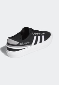 Mustat kanvaslenkkarit, joissa on valkoiset ja harmaat raidat, pyöreä kärki, valkoinen pohja ja logotietoa sivussa. Teksturoitu päällinen ja nyörityssuunnittelu.