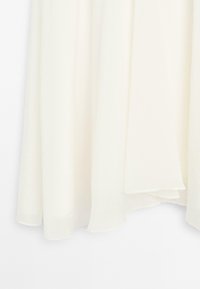 Tissu léger de couleur crème, fluide au toucher doux. L'ourlet présente une coupe asymétrique subtile, mettant en valeur son design léger.