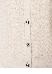 Kremowy sweter o swobodnym splocie z falistą strukturą, zdobiony srebrnymi guzikami i ściągaczem u dołu. Miękki i lekki materiał.