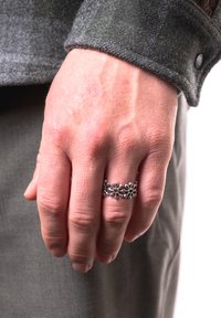 Bague en argent sterling arborant un design floral avec des formes de fleurs et de petites orbites, portée sur une main affichant une texture de peau et des détails visibles.