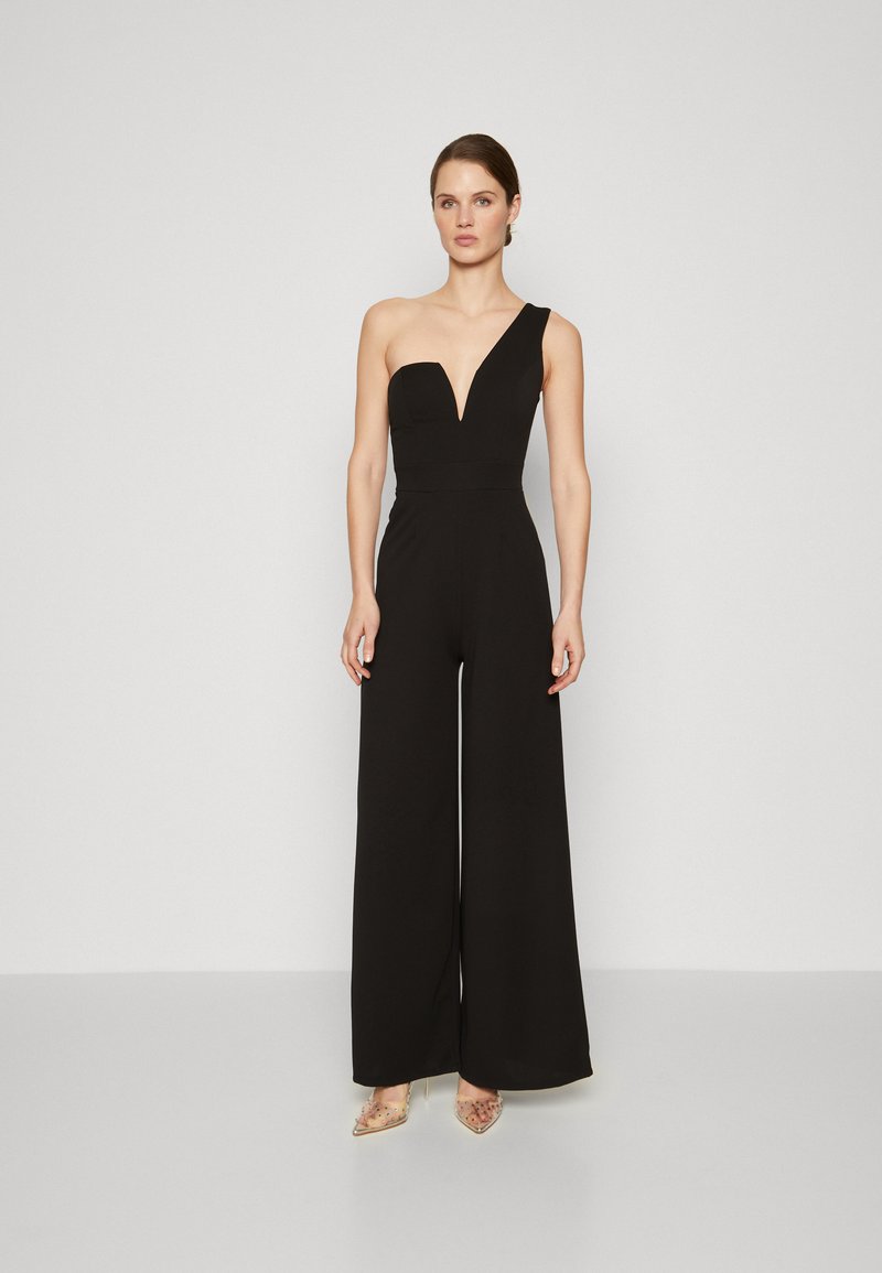 Svart jumpsuit med en skulderdesign og V-hals. Brede ben og en tettsittende overdel. Modellen har på seg sandaler med klar hæl. Glatt, teksturert stoff.