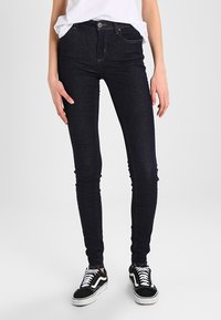 Smalhöga jeans i mörkblå denim med en klassisk femfickdesign och minimala sömnadsdetaljer. I sällskap med svarta sneakers.