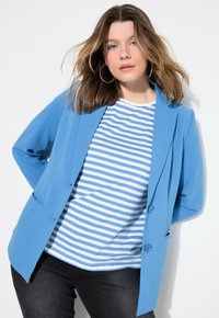 Blazer azul de material suave con un diseño ajustado, combinado con una camiseta de rayas azules y blancas y jeans oscuros.