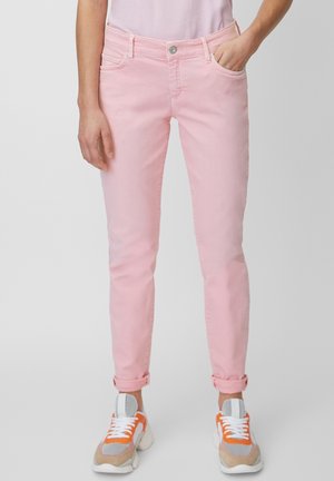 Person iført lyserøde, smalle jeans med opkrogede manchetter, kombineret med hvide, orange og beige chunky sneakers mod en neutral baggrund.