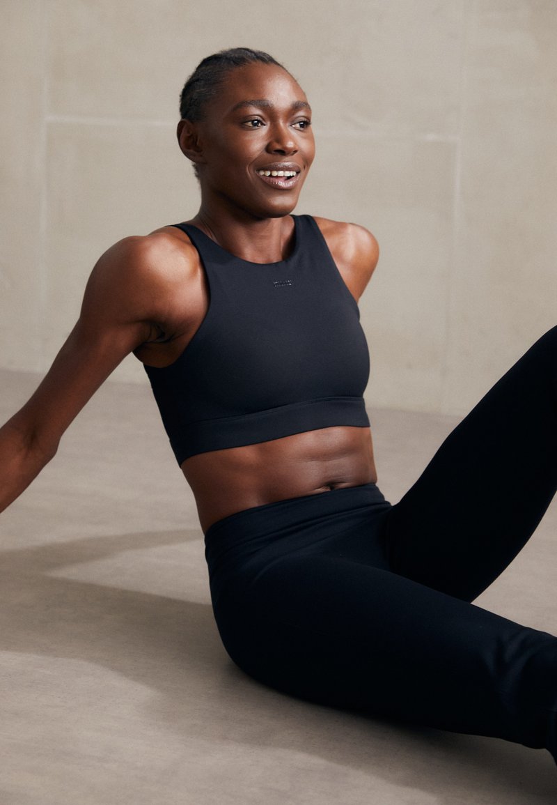 Μαύρο αθλητικό crop top και ψηλόμεσα κολάν φτιαγμένα από λείο, ελαστικό υλικό. Το τοπ διαθέτει σχέδιο racerback και διακριτική σήμανση.