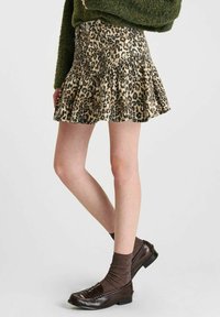 Mini-jurk met luipaardprint en een uitlopende zoom, aangevuld met een bruine gebreide trui en donkere instappers met gestreepte sokken.