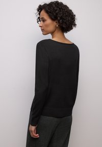 Schwarzer Langarm-Pullover mit weitem Ausschnitt und geripptem Saum. Der Stoff wirkt weich, mit glatter Textur und figurbetontem Schnitt.