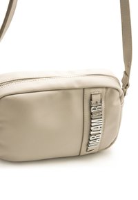 Bolso bandolera de piel beige con cierre de cremallera, que presenta un detalle de logo en relieve en el lateral y una forma rectangular plana.