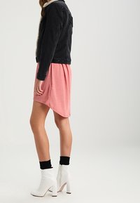 Veste en jean noire avec col en shearling, robe asymétrique rose, chaussettes noires et bottines blanches à zip.