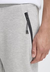 Gray sweatpants with a zippered pocket, featuring a smooth texture and black zipper detail. Elastic waistband with a drawstring.