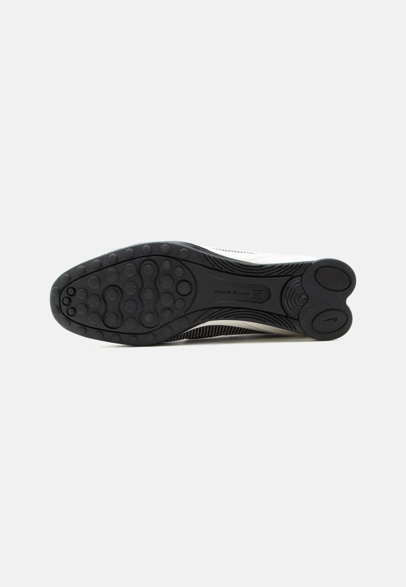 Suela exterior de goma negra de un zapato deportivo blanco que muestra patrones de rodadura circulares y áreas de agarre texturizadas.