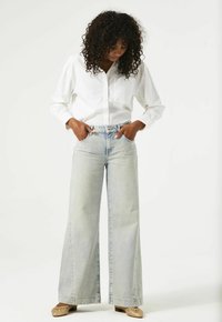 Lichtblauwe wijde jeans van denim, met een hoge taille en een vijf-pocket ontwerp, gecombineerd met een wit langwerpig overhemd met knopen.