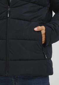 Marineblauer Steppjacke mit Reißverschluss und Seitentasche. Verfügt über ein gestepptes Muster und eine glatte Textur, hergestellt aus leichtem, isolierendem Material.
