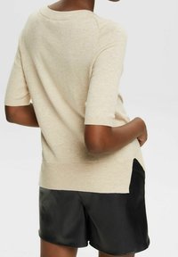 Beige strikket kortærmet sweater med rund halsudskæring, der har en sideslids og en let, struktureret overflade. Matchet med sorte shorts.