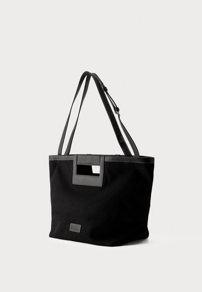 Μαύρη τσάντα tote με διπλές λαβές, ορθογώνιο άνοιγμα κοντά στην πάνω άκρη, αντίθετη ραφή και μικρό μπροστινό λογότυπο.