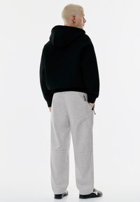 Sort cropped hættebluse med hætte, parret med lysegrå sweatpants med lommer og en afslappet pasform. Glat tekstur, minimalistisk design.