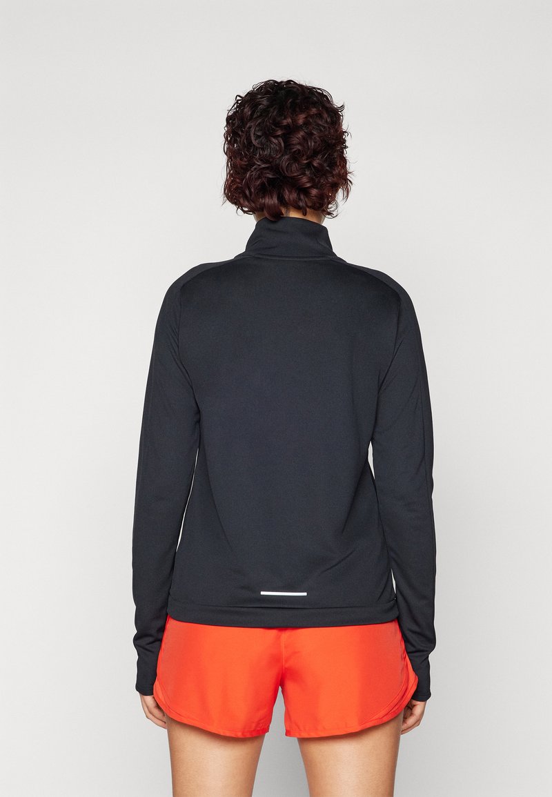 Camiseta atlética negra de manga larga con un alto cuello, combinada con pantalones cortos atléticos rojos. Textura suave con detalles reflectantes en el dobladillo.