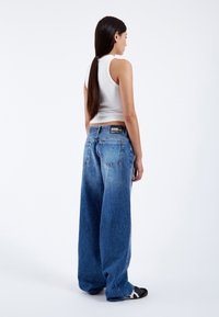 Lichtblauwe wijde denim jeans met een vervaagde textuur en achterzakken. Zwarte label op de tailleband. Eenvoudig wit tanktop zichtbaar.
