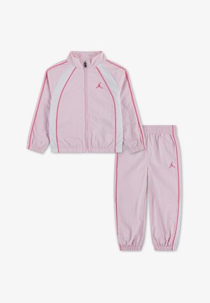 Ensemble de survêtement deux-pièces rose clair avec panneaux blancs et bordures roses, comprenant une veste zippée et un pantalon à poignets élastiques avec un petit logo sur la poitrine et la cuisse.