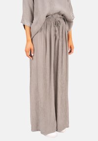 Pantalons large gris clair avec une finition texturée, dotés d'une taille élastique et d'un cordon de serrage, associés à des baskets blanches.