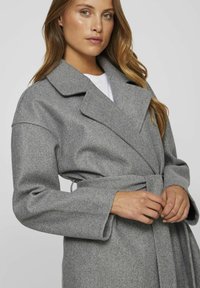 Cappotto di lana grigio con vita a fascia, ampi revers e maniche lunghe. Finitura testurizzata e design con apertura frontale.