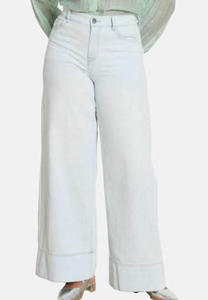 Jasnoniebieskie jeansy o szerokich nogawkach i wysokim stanem, z przednimi kieszeniami, noszone ze srebrnymi butami na niskim obcasie i włożonym do środka teksturowanym zielonym topem.