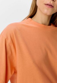 Camiseta de manga corta color naranja claro, hecha de algodón suave. Presenta un escote redondo y un corte relajado con una textura suave.