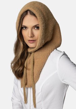 Béžový svetrový šátek s kapucí a žebrovanou strukturou, s prodlouženými šňůrkami a měkkým, luxusním vzhledem. Stylizováno s bílým topem.