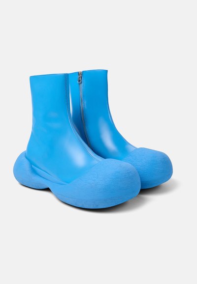 Stivali alla caviglia blu con una finitura liscia e lucida, chiusura con zip, punta tonda e suole grobate spesse. Realizzati in materiale sintetico resistente.