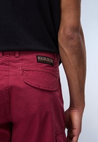 Pantaloni cargo rossi in cotone con tasca posteriore, caratterizzati da un'etichetta ricamata "Napapijri Geographic" e dettagli di cucitura visibili.