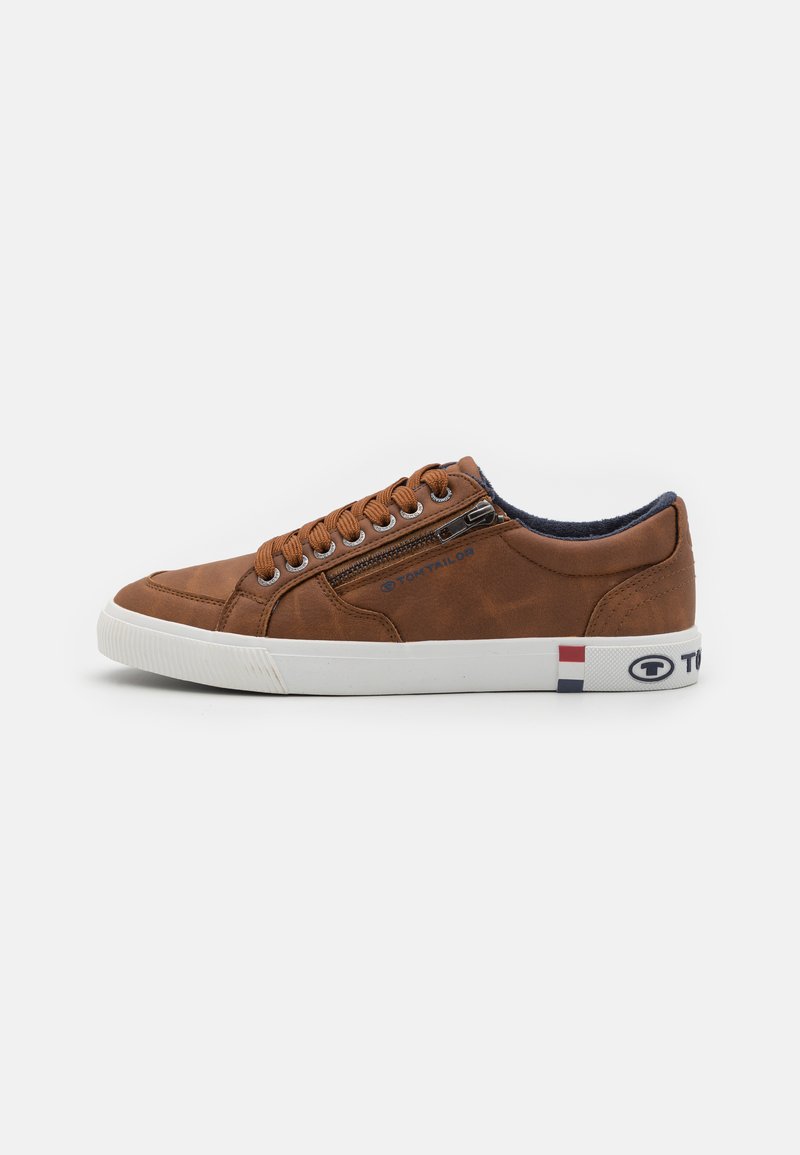 Baskets en cuir marron avec semelle en caoutchouc blanche, à lacets à l'avant, fermeture éclair sur le côté, et accents de logo en rouge, blanc et bleu au niveau du talon.
