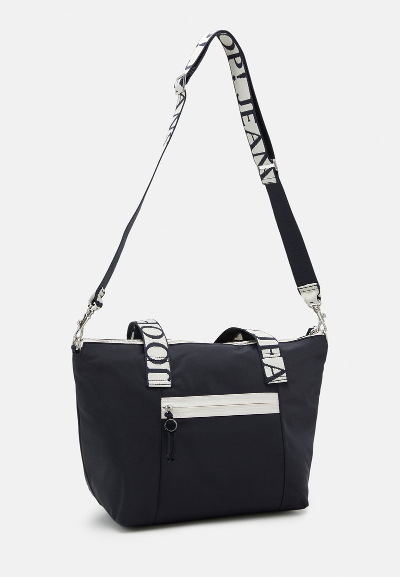 Schwarze Nylon-Shopper-Tasche mit zwei Griffen und einem verstellbaren Riemen. Sie verfügt über eine weiße Reißverschlusstasche auf der Vorderseite und gestreifte textile Akzente.
