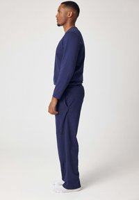 Marineblauw T-shirt met lange mouwen en bijpassende broek van zachte stof, voorzien van een ontspannen pasvorm en elastische tailleband, gedragen met witte sokken.