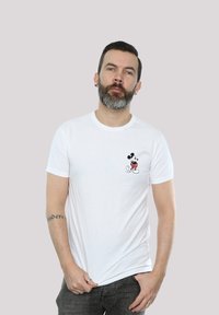 Hvit bomull T-skjorte med en liten svart og rød Mickey Mouse-grafikk på venstre bryst. Kortermet med rund halsdesign.