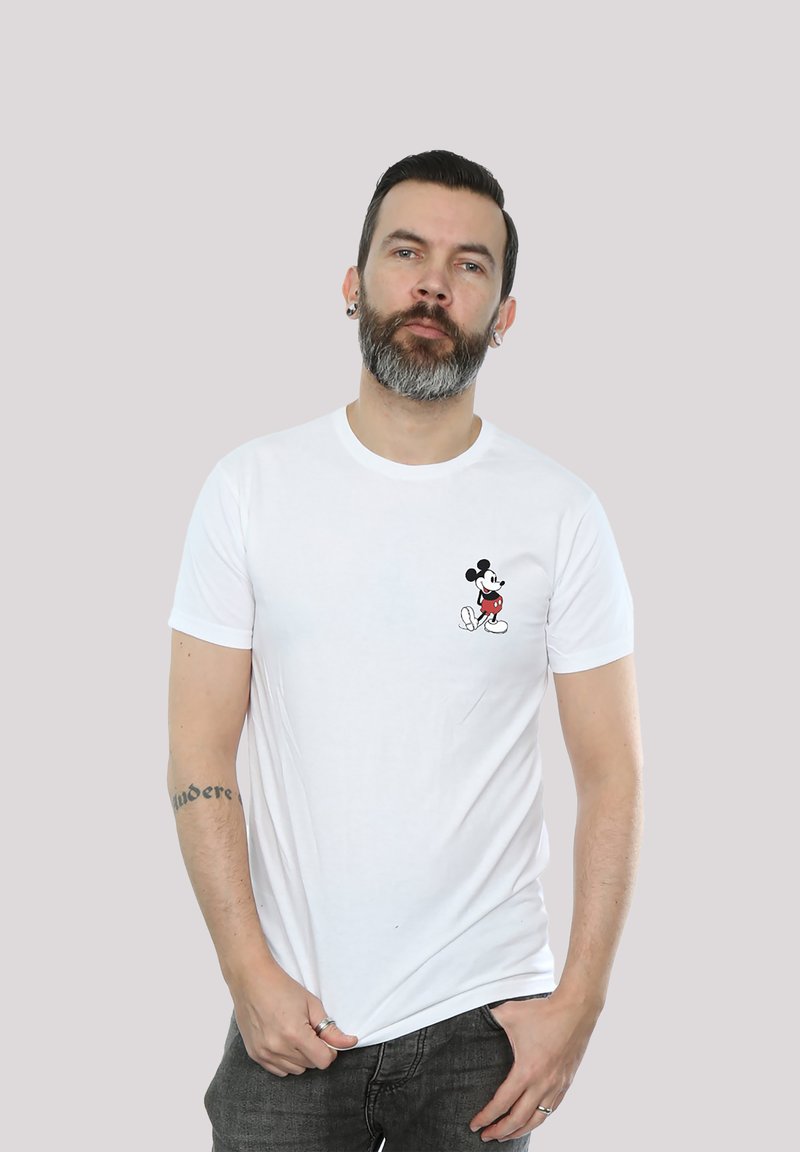 Hvit bomull T-skjorte med en liten svart og rød Mickey Mouse-grafikk på venstre bryst. Kortermet med rund halsdesign.
