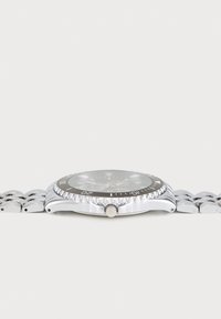 Silver metal watch with a round black face, textured bezel, and linked bracelet. Features a prominent crown on the side.