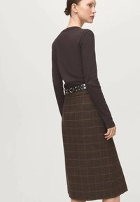 Hnedý dlhý rukáv top v kombinácii s hnedou midi sukňou s károvaným vzorom, obsahujúcim oranžové a zelené pruhy, doplnený čiernym opaskom so striebornými cvočkami.