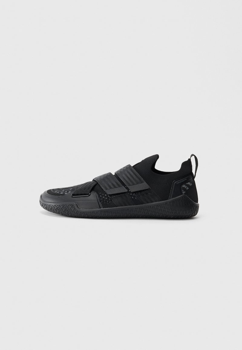 Black slip-on sneaker with textured sole, two wide hook-and-loop straps, knit upper, and pull tab at heel on a plain background.