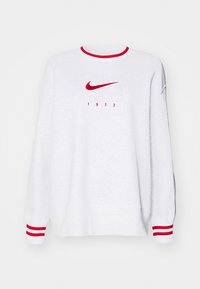 Felpa bianca con dettagli rossi, collo tondo e polsini a coste con logo Nike ricamato in rosso e "1972" sotto.