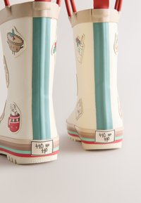 Gummistiefel mit einer cremefarbenen Basis, einem türkisfarbenen Streifen, weihnachtlich gestalteten Aufklebern und mehrfarbigen horizontalen Akzenten an der Sohle.