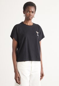 Sort bomulds t-shirt med korte ærmer og løs pasform. Har et lille design med en pailletbelagt martiniglas på venstre bryst. Samlet med hvide bukser.