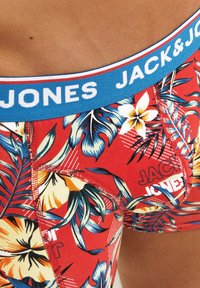 Rote Boxershorts mit floralem Muster, ausgestattet mit einem blauen Bund, auf dem "JACK & JONES" in Weiß gedruckt ist. Enthält dekorative Nähdetails.